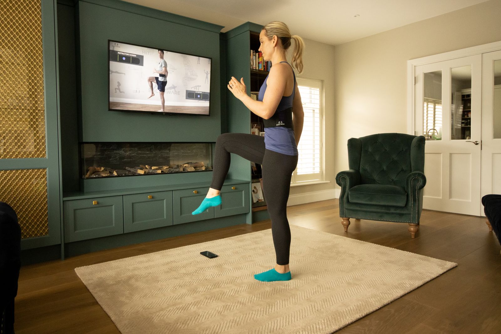 A woman balancing on one leg with the other extended behind her, following a class on the television.